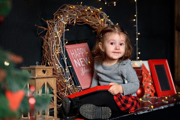 Niña sentada cerca del árbol festivo y la guirnalda