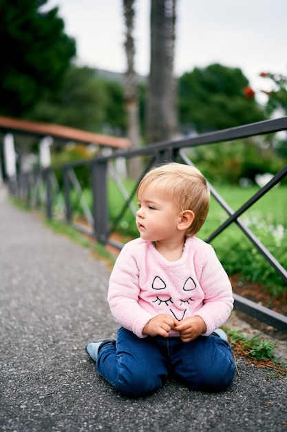 Niña sentada cerca de una valla metálica en un parque verde