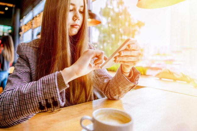 Una niña sentada cerca de la ventana tocando en la pantalla del teléfono inteligente