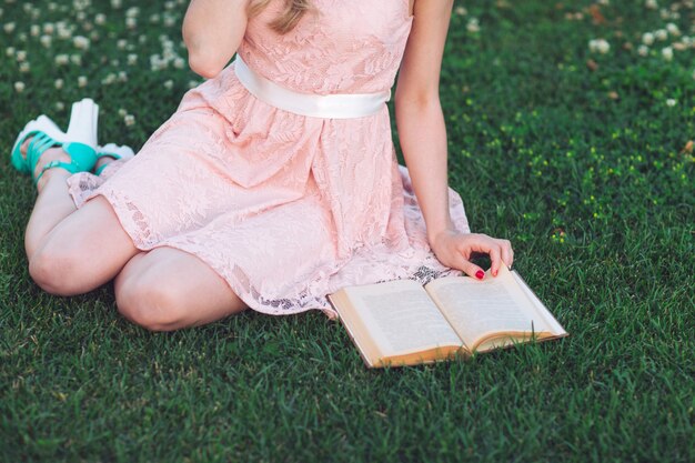 Una niña sentada en el césped y leyendo un libro.