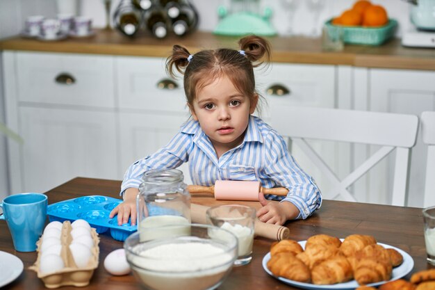 Niña sentada en la cocina en la mesa y va a rodar la masa.