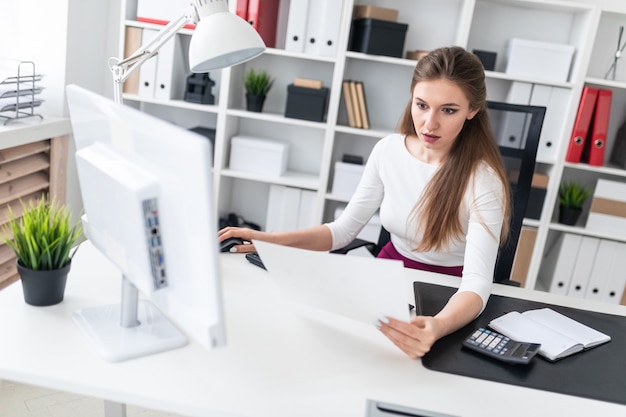 Una niña sentada en una computadora de escritorio y trabajar con documentos.