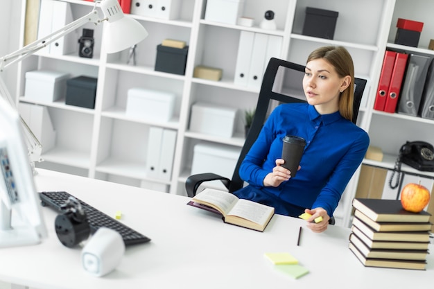 Foto una niña sentada en el escritorio de una computadora y sostiene un vaso con café