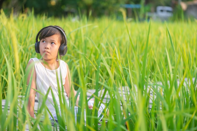 niña sentada y escuchando música en el puente de madera en el campo de arroz en la puesta del sol