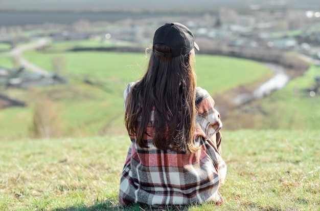 Una niña sentada con la espalda en una colina disfruta de una hermosa vista