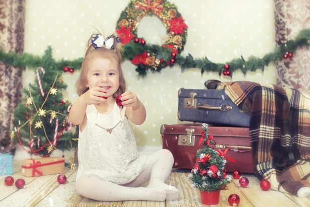 Niña sentada frente a un árbol de Navidad y jugando con juguetes