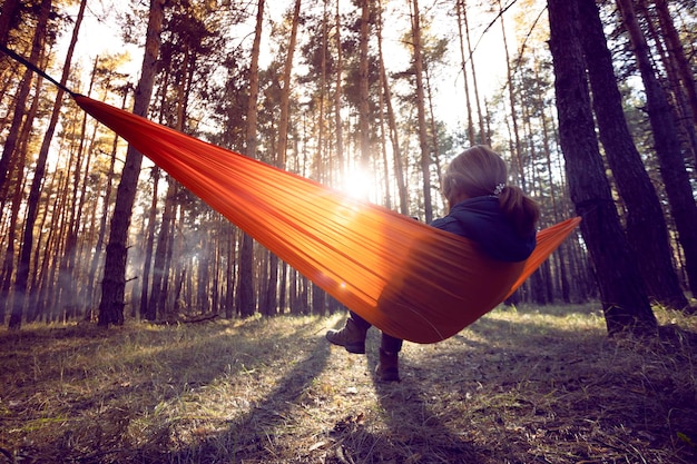 Niña sentada en una hamaca naranja al atardecer en el bosque