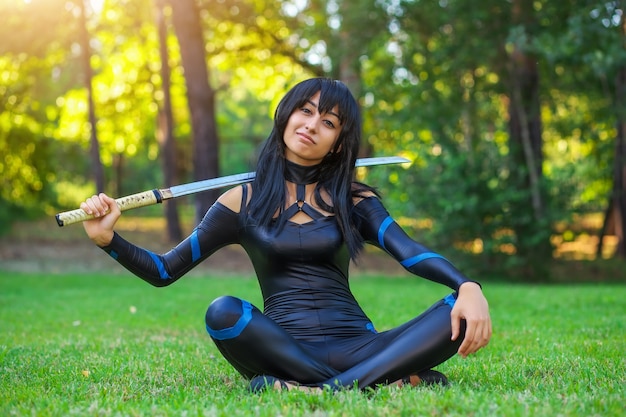 Niña sentada en la hierba y sosteniendo la espada samurai. Personaje de cosplay original