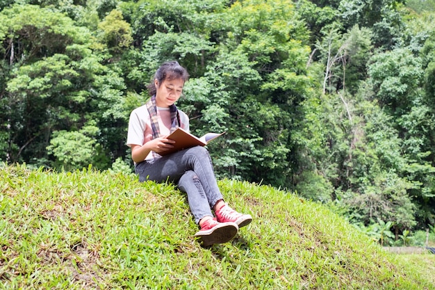 niña sentada en la hierba verde en el parque y leyendo un libro.