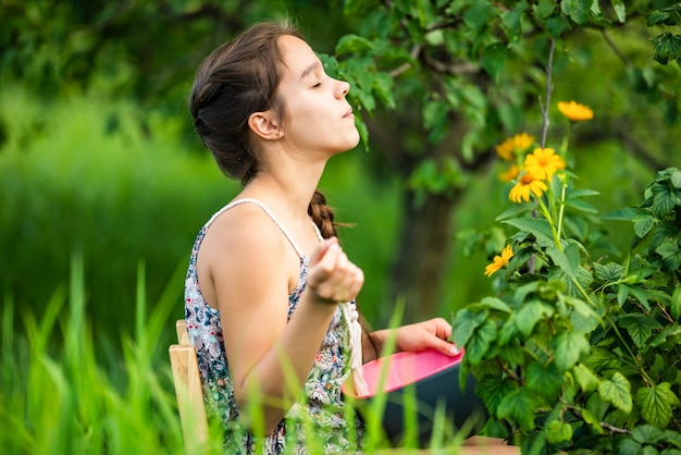 Una niña sentada en un jardín cerca de un arbusto con flores.