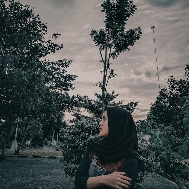 Foto niña sentada junto al árbol contra el cielo