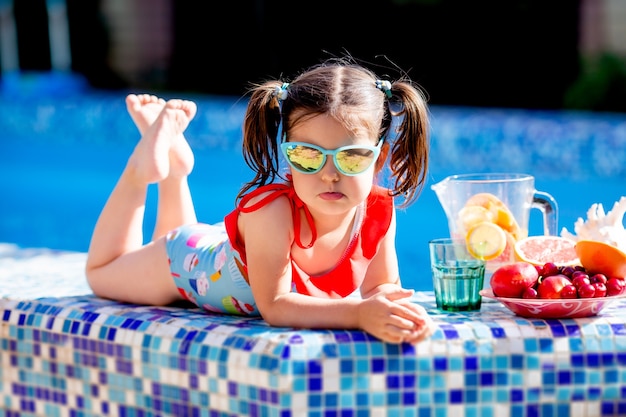 Niña sentada junto a la piscina bebiendo limonada