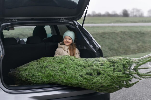 Niña sentada en el maletero con un árbol de Navidad