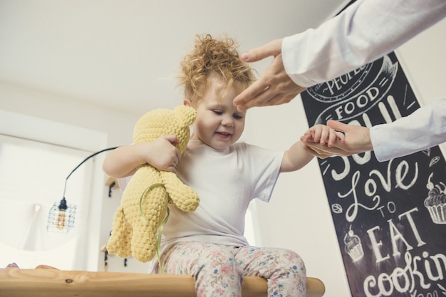 Niña sentada en la mesa y abrazos de juguete. Concepto de cuidado familiar.