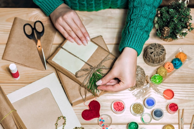 Niña sentada en la mesa envuelve regalos de Navidad