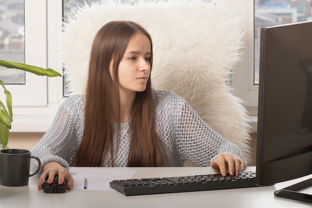 Niña sentada en una mesa, escribiendo en una computadora