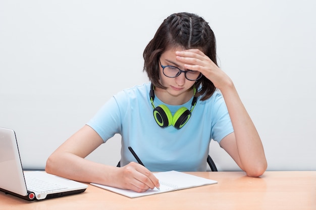 Foto niña sentada en una mesa, escribiendo la tarea.