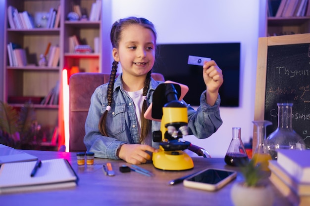 Niña sentada en la mesa mirando una diapositiva del microscopio