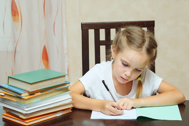 Niña sentada a la mesa con pila de libros y hacer los deberes