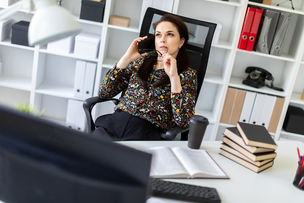 Una niña sentada en la oficina en la computadora Escritorio y hablando por teléfono.