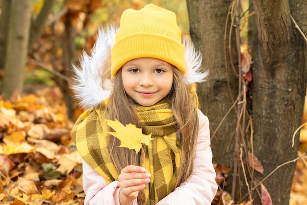 Niña sentada en otoño hojas caídas en el bosque.