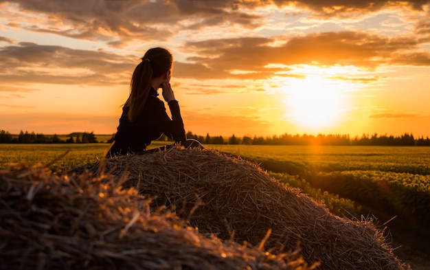 Niña sentada en un pajar en un campo al atardecer