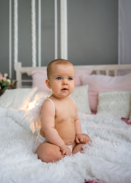 Niña sentada en un pañal y con alas de ángel en la cama