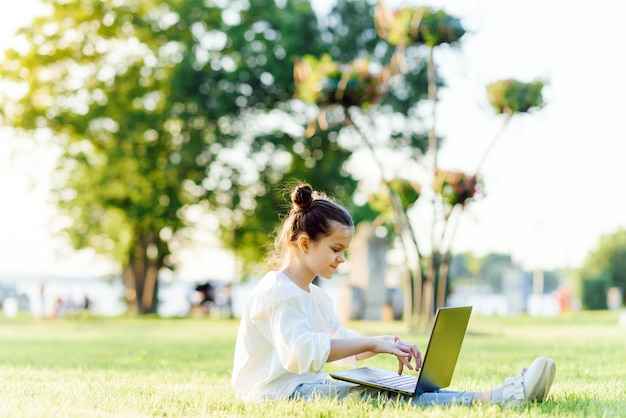 Niña sentada en el parque y trabajando con ordenador portátil. Educación, estilo de vida, concepto de tecnología