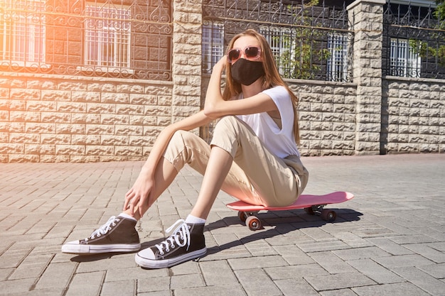 La niña sentada en patineta Paisaje de la ciudad Mascarilla negra reutilizable