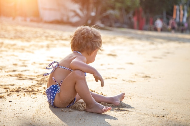 Niña sentada en una playa de arena bajo el sol