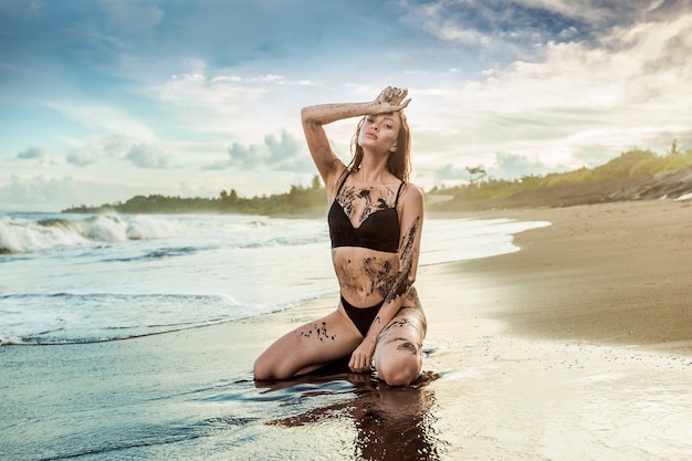 Foto la niña sentada en la playa y manchada de arena negra.