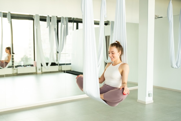 Niña sentada en una posición de loto en una hamaca para yoga aéreo haciendo relajación mudras en clases de yoga