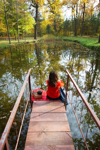 Foto niña sentada en el puente de madera por el lago