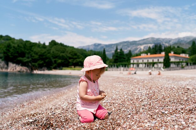 Niña sentada de rodillas en la playa junto al agua villa milocer