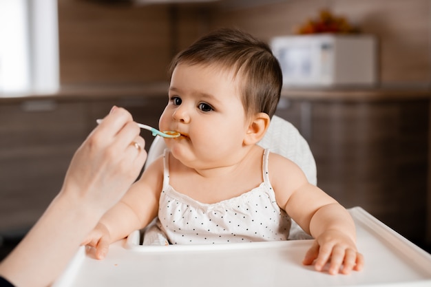 Niña sentada en la silla de un niño comiendo puré de verduras