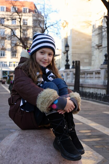 Niña sentada sobre una esfera de piedra en la clara mañana de otoño. Paisaje de la ciudad al fondo