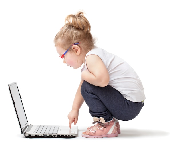 Niña sentada sobre fondo blanco y jugando con una computadora portátil