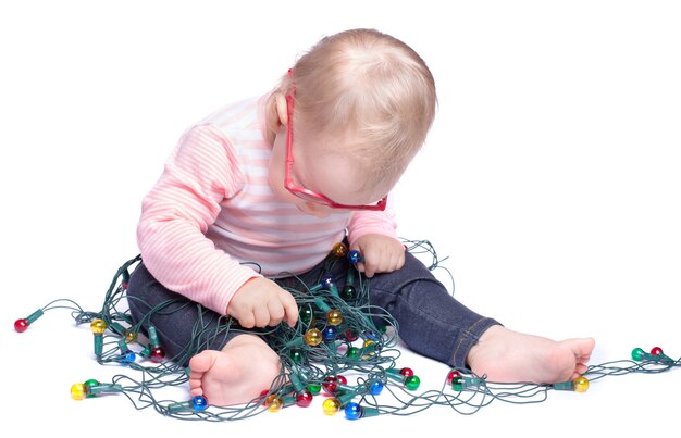 Niña sentada sobre fondo blanco y jugando con luces de Navidad. Aislado en blanco