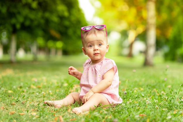 Niña sentada sobre la hierba verde en un traje rosa y gafas brillantes, caminando al aire libre