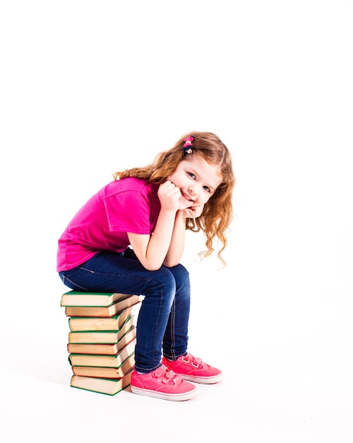 Niña sentada sobre una pila de libros antiguos, sosteniendo su cabeza y mirar aislado en blanco