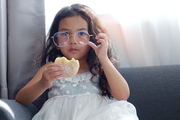 Niña sentada en el sofá comiendo donut