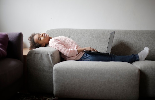 niña sentada en un sofá en el interior con una computadora portátil