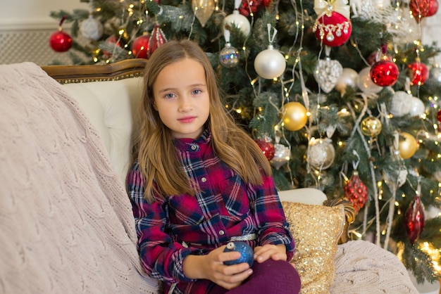 niña sentada en el sofá en navidad en el fondo de un árbol de navidad en casa