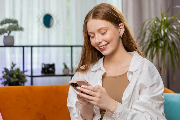 Niña sentada en el sofá usando su teléfono inteligente compartiendo mensajes en la aplicación de redes sociales viendo películas