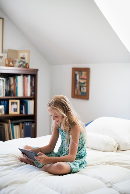 Una niña sentada en su cama usando una tableta digital