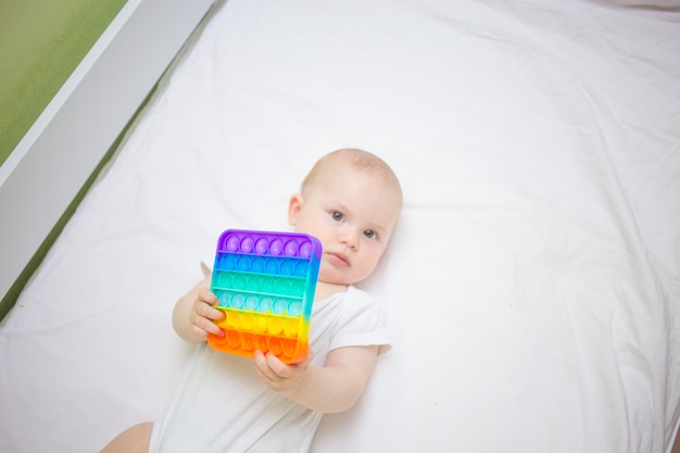 Niña sentada en su casa en la cama, jugando Pop-it nuevo juguete antiestrés, popular entre los niños. Idea de desarrollo infantil.