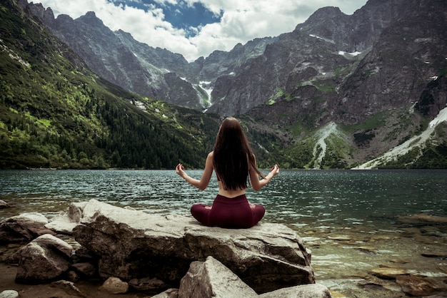 Foto niña sentada en sukhasana posan en piedra grande frente al lago de montaña