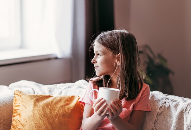 Niña sentada con una taza blanca en el sofá de la sala de estar