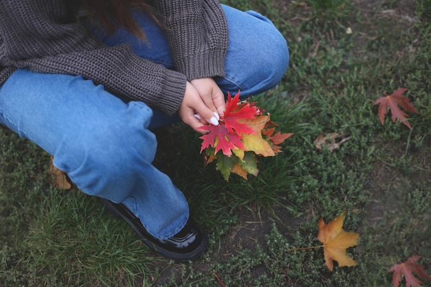 la niña se sentó y tiene hojas secas en sus manos