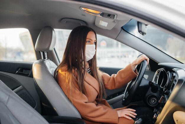 Una niña se sienta al volante en el automóvil con la máscara durante la pandemia mundial y el coronavirus. Cuarentena